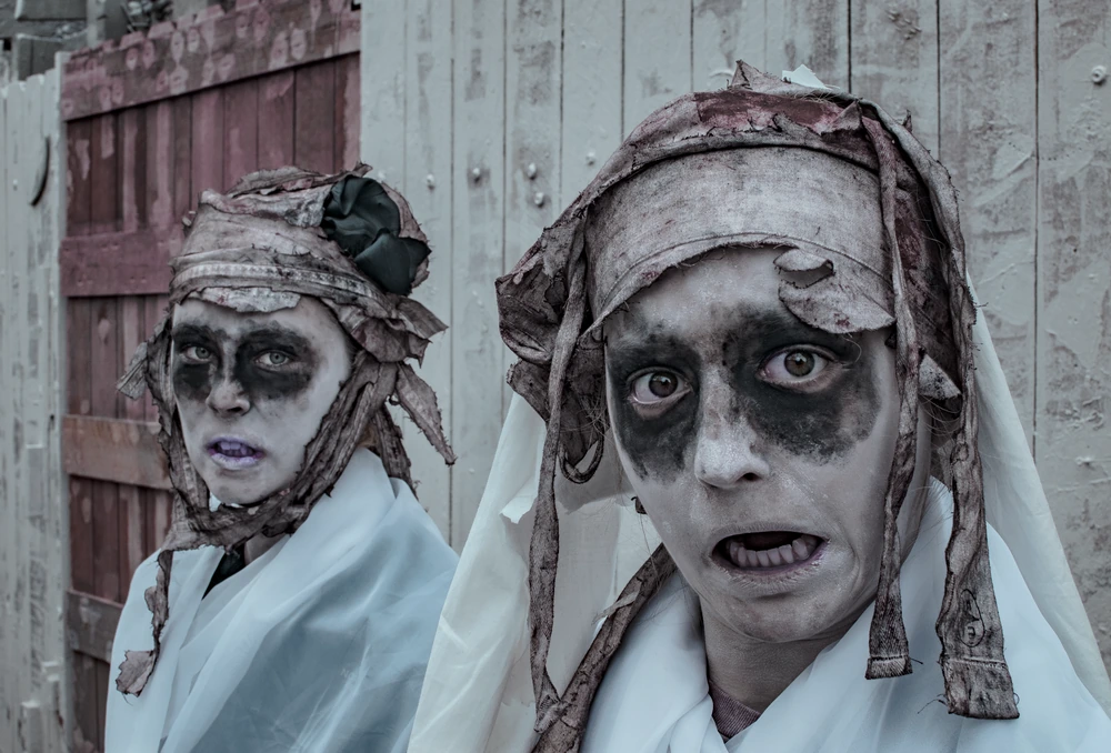 Two figures, bandaged and masked, against a weathered fence